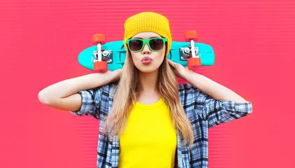 Meubelstickers Portrait cool woman with skateboard wearing colorful yellow hat on pink background © rohappy