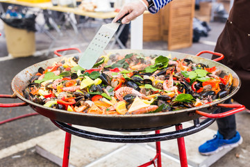 Street food concept - Gourmet seafood paella with pink marine prawns and mussels on yellow saffron rice with peas and bell peppers