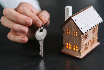 house keys in the hands of a woman and a small model of a house with luminous windows nearby. concept of acquiring your home
