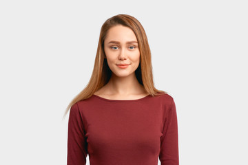 Obraz premium Sweet looking girl looks at camera, gentle soft smile, self confidence. Beautiful young woman with long hair, clean smooth skin wears Burgundy-colored jacket sleeves isolated on background in Studio