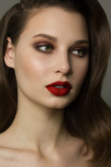 Fototapeta premium Close-up portrait of the cleanliness face of a beautiful woman with dark black smoky eyes makeup, red full lips. Sexy model with clean shiny skin, clean face, long curly hair. glamorous image
