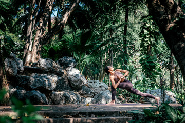 Live in the moment. Full-length shot of caucasian woman standing in Crescent Lunge Twist pose, while practicing yoga outdoors, in a garden. Healthy lifestyle and relaxation concept