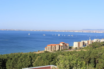 View from the top of the mountain covered with green trees on the blue sea Bay with a sailing regatta