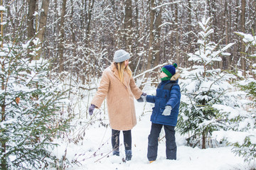Fototapeta na wymiar Parenting, fun and season concept - Happy mother and son having fun and playing with snow in winter forest