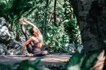 Move, stretch, strengthen. Full-length shot of caucasian woman sitting in Seated Hand to Big Toe pose, while practicing yoga outdoors, in a garden. Healthy lifestyle and relaxation concept