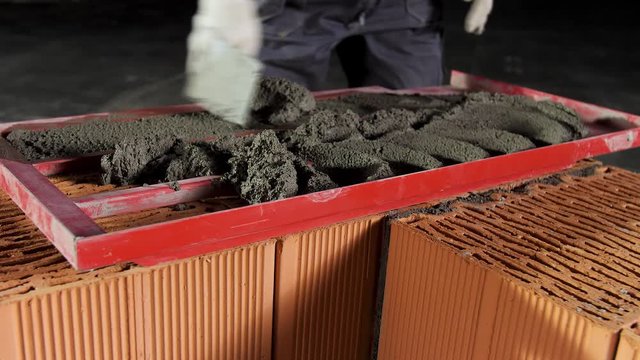 Close up of a worker putting mortar into the wooden frame to make a layer on the brick wall. Stock footage. Levelling of cement at the constructtion site.