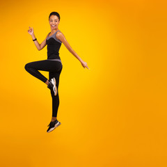 Fototapeta na wymiar African American Lady Jumping Over Yellow Studio Background