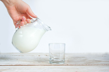 Female hand holds kefir in a glass jug on a white background. The concept of diet and healthy eating. Fermented dairy products.