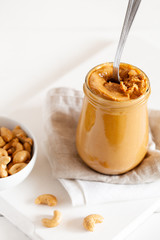 Homemade natural paleo nut peanut cashew creamy butter in glass jar and spoon on white background.Vertical orientation