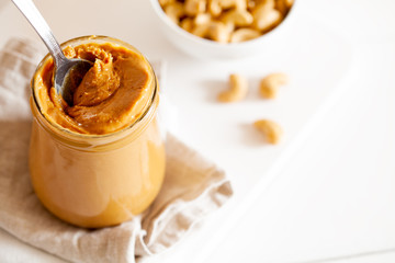 Homemade natural paleo nut peanut cashew creamy butter in glass jar and spoon on white background...