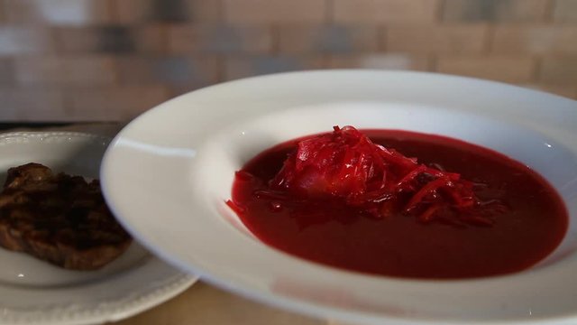 Borsch in a white plate, next to sour cream and fried meat.Borscht.The process of pouring traditional Russian borsch soup into a clean white plate.
