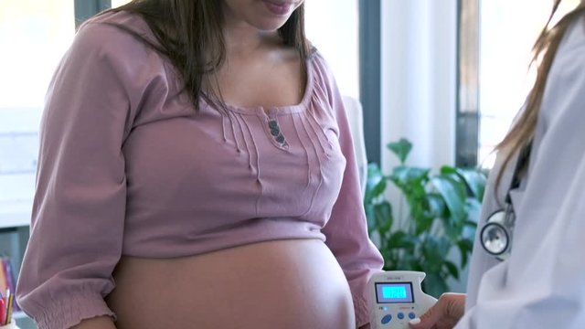 Obstetrician gynecologist performing Doppler auscultation checking blood flow in placenta and uterus in the clinic.