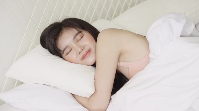 Beautiful asian young woman sleeping lying in bed with head on pillow comfortable and happy in the bedroom moving panning camera, girl with relax and leisure for health, lifestyle concept.