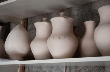 Fototapeta na wymiar Handmade ceramic ceramics with glaze and without glaze. Pitchers and pots dry on shelves in a pottery workshop before the firing process.