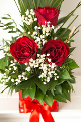 Closeup on a handmade red box with floral arrangement. The flower arrangement consists of three red roses and green leaves. A wonderful gift for a woman.