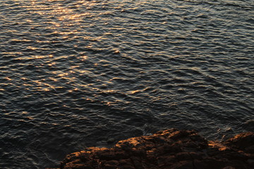 Detail of rock and dark blue sea with golden twilight reflections