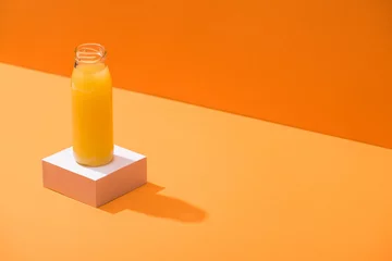 Poster Im Rahmen fresh juice in glass bottle on white cube on orange background © LIGHTFIELD STUDIOS