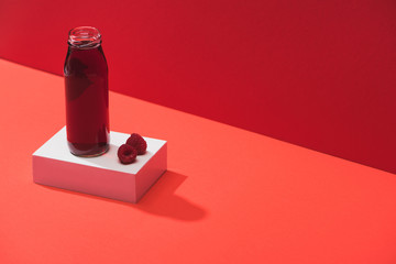 fresh berry juice in glass bottle near ripe raspberries on cube on red background