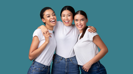 Fototapeta premium Three Happy Diverse Girls Hugging On Turquoise Studio Background, Panorama