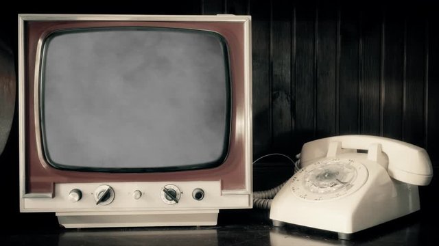 Analog scene with a rotary phone and a vintage TV showing grey smoke rising over a black background.