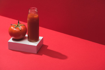 fresh vegetable juice in glass bottle and ripe tomato on cube on red background