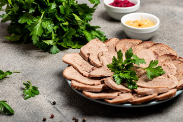 Boiled beef tongue with greens on a plate. Close-up.