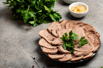 Boiled beef tongue with greens and mustard on a plate. Close-up. Copy space for text.