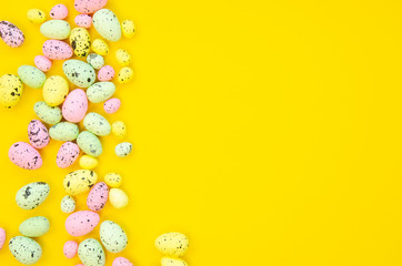 Festive Easter border made of painted quail eggs isolated on yellow. Copy space, top view