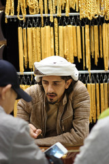 Arab jeweler haggling with asian customers. He's showing them some gold jewelry