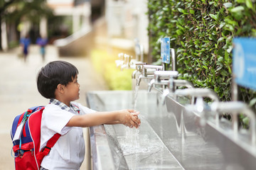 An Asian school boy washing his hand at an outdoor faucet sink and water tab in a school.