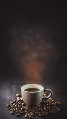  cup of coffee and coffee grains with smoke on a dark background.