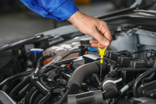 Male mechanic checking level of oil in car engine
