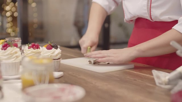 Tilt up of female chef wearing uniform cutting pieces of chocolate while standing at worktop in kitchen