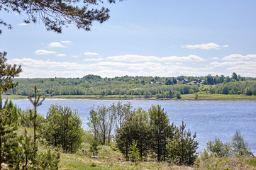 Summer landscape of a river bank, with green forest and village buildings