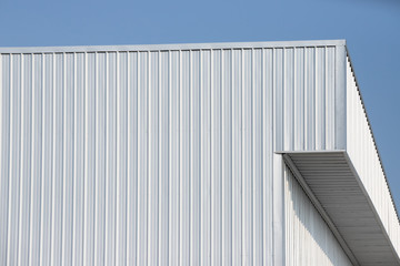 metal sheet factory warehouse against blue sky background. silver corrugated steel industrial roof.