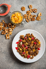 Granola with dried fruits in a white plate on a gray background. Close-up. Open decorative jar with dried fruits. Top view.