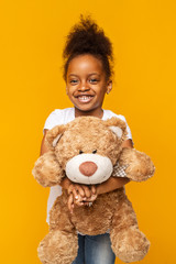 Pretty afro girl holding teddy bear over yellow background