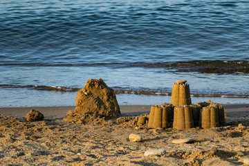  Children's sand figurines on the beach. Buildings made of water, sand and stones, illuminated by sunlight from the side, at sunset, a beautiful photo for memory