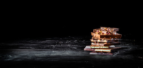 Hazelnut and almond milk and dark chocolate pieces tower on dark background