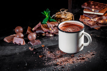 Portion of homemade mint hot chocolate in a cup with chocolate and nuts on dark background