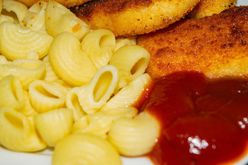 Fried chicken nuggets and boiled pasta with ketchup on a plate. Close up.
