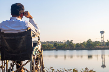 Young disabled man with field background.He is wearing a hat and sitting on wheelchair.He is...