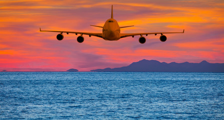 Airplane flying above tropical sea at sunset