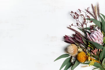 Muurstickers Mooi platliggend bloemstuk van voornamelijk Australische inheemse bloemen, waaronder protea, banksia, kangoeroepoot eucalyptusbladeren en gomnoten op een witte achtergrond. Ruimte voor kopiëren. © tegan