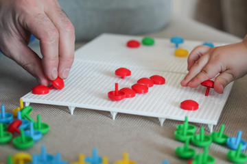 Child playing with mushroom nail mosaic. Father and baby playing together concept. Educational toy DIY puzzle. Colorful jigsaw pegboard. Toddler's hand with bright creative toy. Hobby and leisure time