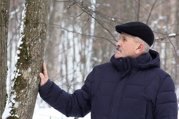 Aged man touching tree stem and looking at stem in the winter forest