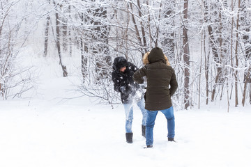 Fototapeta na wymiar Lifestyle, season and leisure concept - Funny couple playing snowball in winter park