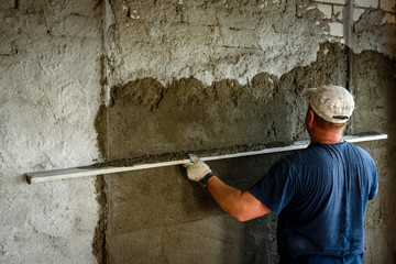 Construction worker plastering wall with leveler.