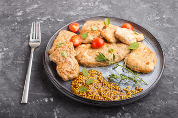 Fried pork chops with tomatoes and herbs on a gray ceramic plate on a black concrete background. side view.