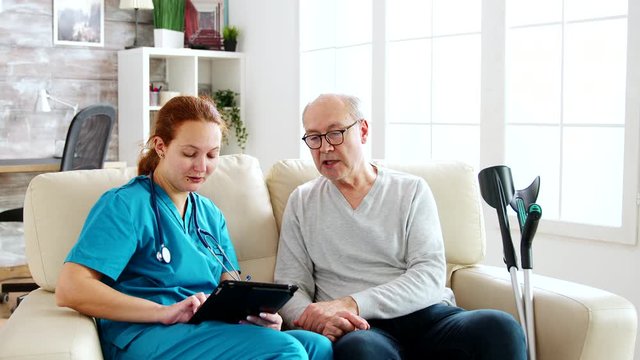 Female caucasian nurse taking notes about elderly man health in bright and cozy nursing home
